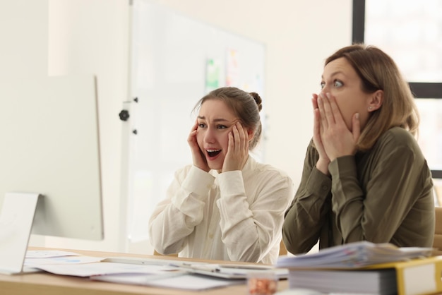 Le manager donne scioccate guardano il monitor del computer ai colleghi della scrivania colpiti da online