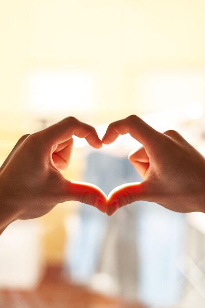 le mani a forma di cuore contro il cielo passano i raggi del sole. Mani a forma di cuore d'amore