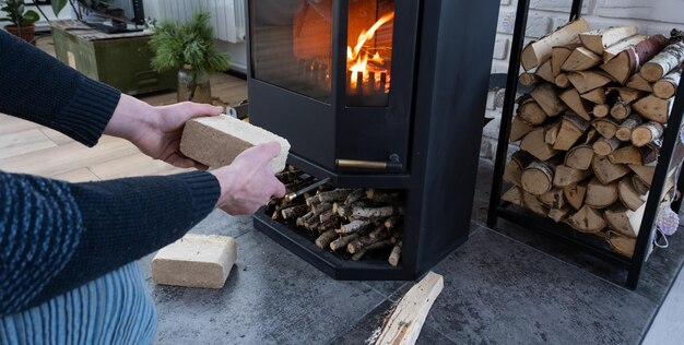 Le mani accendono il focolare con bricchetti economici Bricchetti combustibili fatti di segatura pressata per accendere la fornace alternativa economica combustibile ecologico per il camino in casa