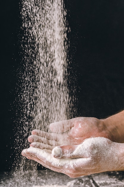 Le mani adulte dell'uomo funzionano con farina, foto scura