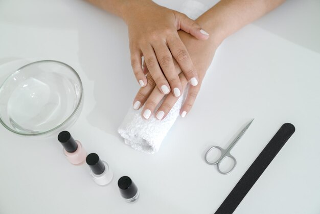 Le mani ben curate delle donne con la manicure bianca giacciono sul tavolo, gli accessori per manicure sono accanto