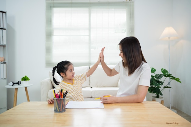 Le mani carine del bambino e della mamma mi danno il cinque mentre dipingono con colori colorati Ragazza asiatica e madre che usano i pastelli a colori Figlia e mamma che fanno i compiti colorando i personaggi dei cartoni animati