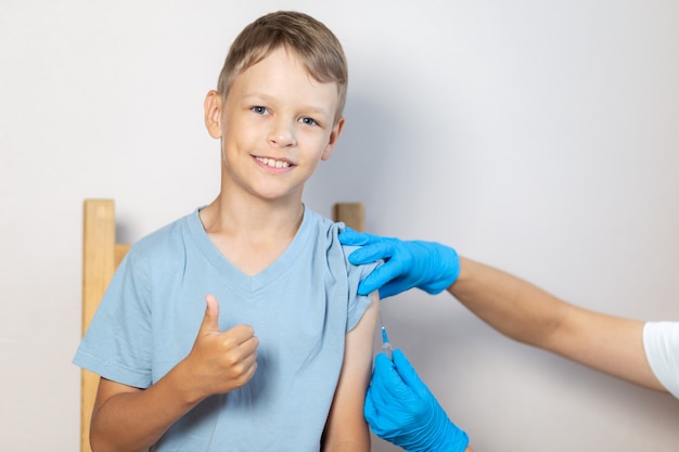 Le mani degli infermieri in guanti blu iniettano il vaccino attraverso una siringa nella spalla dei ragazzi