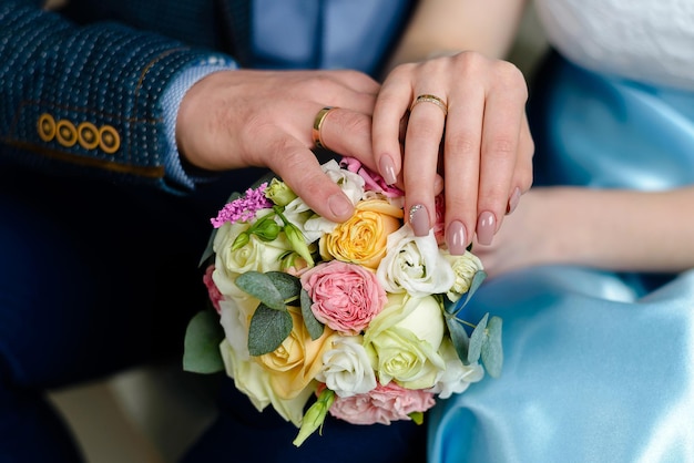 le mani degli sposi con anelli si tengono per mano con un bouquet