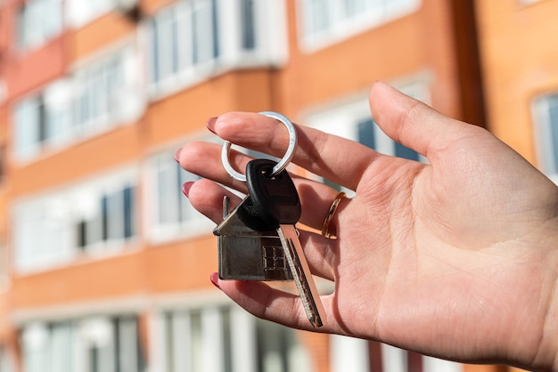 Le mani degli uomini che tengono la chiave con un portachiavi a forma di casa sullo sfondo di una casa fresca