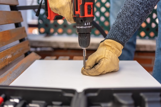 Le mani degli uomini che tengono una vite per avvitarla con una macchina elettrica alimentata a batteria in un legno