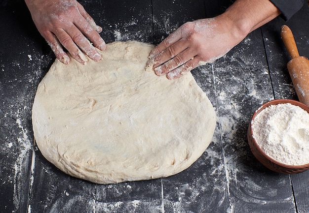 Le mani degli uomini impastano un pezzo rotondo di pasta