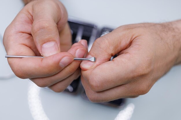 Le mani degli uomini puliscono la cuticola vicino all'unghia con uno strumento Un uomo si fa una manicure