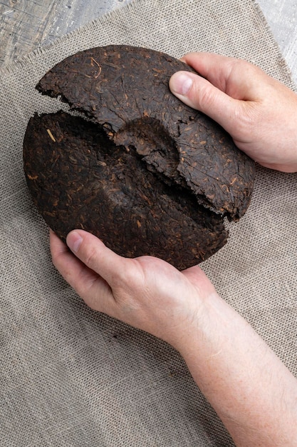 Le mani degli uomini rompono un disco di tè puerh cinese pressato nero