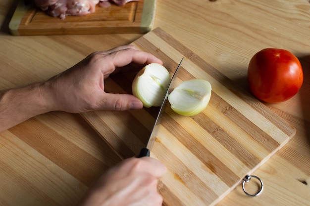 Le mani degli uomini tagliano le cipolle su una tavola di legno