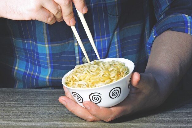 Le mani degli uomini tengono le tagliatelle con le bacchette. Tagliatelle cinesi, bastoncini, mani.