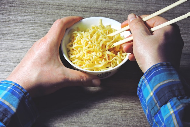 Le mani degli uomini tengono le tagliatelle con le bacchette. Tagliatelle cinesi, bastoncini, mani.