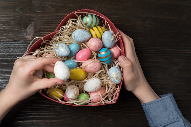 Le mani dei bambini che tengono il cuore hanno modellato la scatola con le uova di Pasqua variopinte. Concetto di regalo di Pasqua