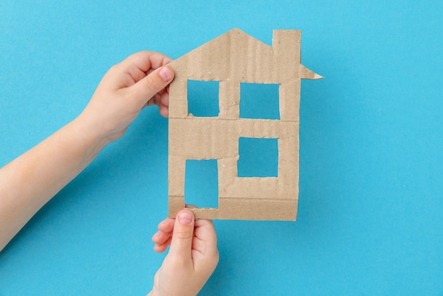 Le mani dei bambini che tengono una casa di cartone su sfondo blu