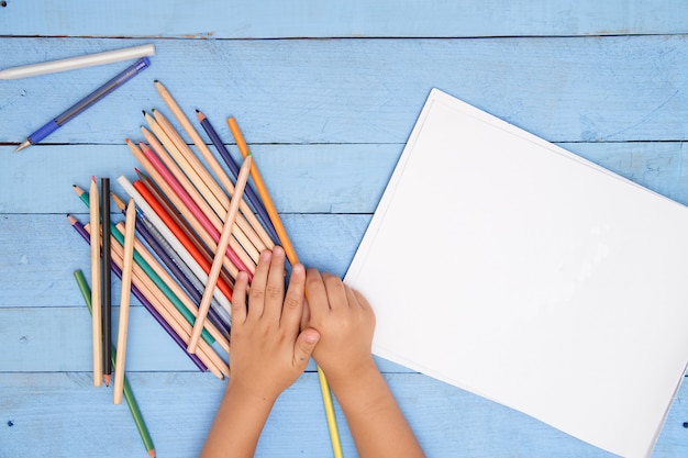 Le mani dei bambini disegnano con le matite nell'album sul tavolo blu