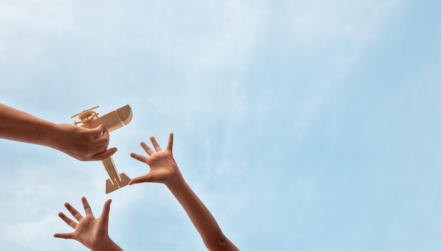 Le mani dei bambini e le mani del padre che giocano l'aereo di legno giocano su un bello cielo