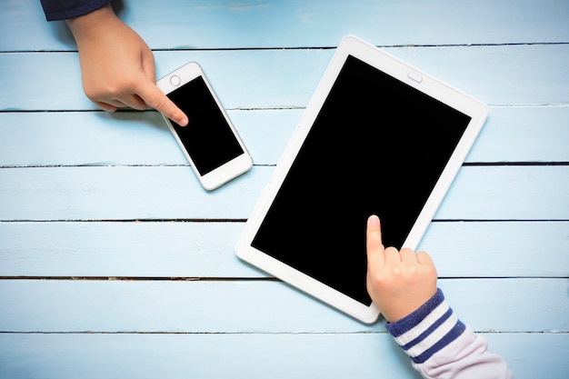 Le mani dei bambini facendo uso del computer della compressa sulla tavola blu di legno.