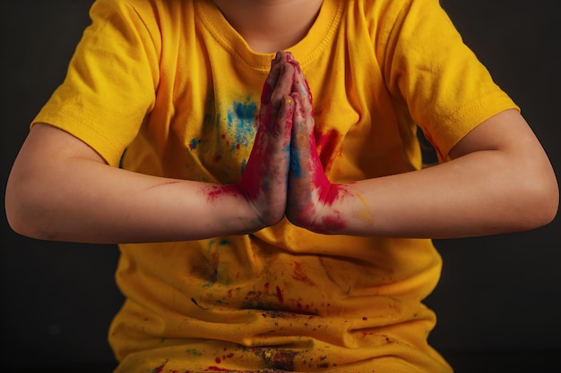 le mani dei bambini in vivaci colori Holi multicolori sono piegate in un gesto di saluto Namaste