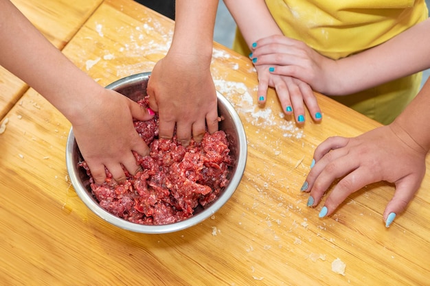 le mani dei bambini mescolano la carne macinata in una ciotola su un tavolo di legno