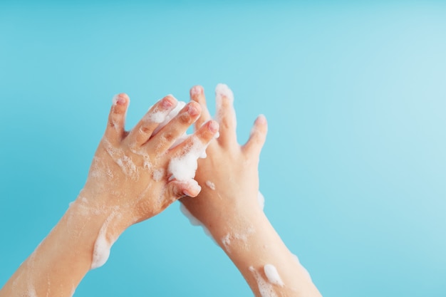 Le mani dei bambini nella saponata del sapone, su un primo piano blu della parete, vista superiore.