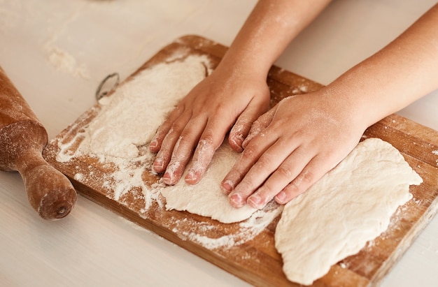 Le mani dei bambini si trovano sopra l'impasto arrotolato su una tavola di legno