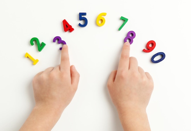 Le mani dei bambini spostano i numeri su un tavolo bianco Imparare i colori e contare da zero a dieci