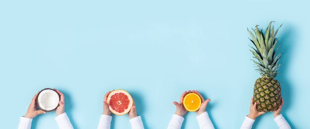 Le mani dei bambini tengono cocco, pompelmo, arancia e ananas intero su sfondo blu