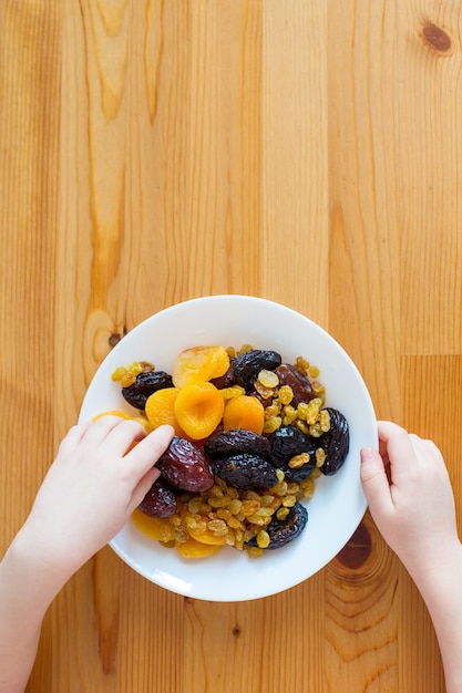 Le mani dei bambini tengono un piatto con frutta secca. Cibo sano, vitamine