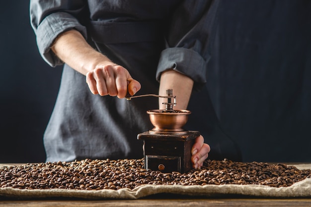 Le mani dei baristi in un grembiule scuro macinano su un macinino manuale fragranti chicchi di caffè