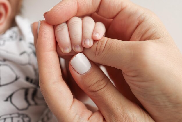 Le mani dei genitori tengono le dita di un neonato La mano di una madre e di un padre da vicino tiene il pugno di un neonato Salute familiare e assistenza medica Foto professionale su sfondo bianco