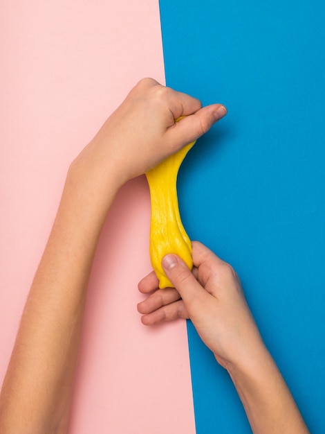 Le mani del bambino allungano una melma gialla su uno sfondo rosa e blu. Giocattolo antistress. Giocattolo per lo sviluppo delle capacità motorie manuali.