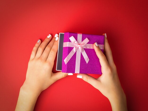 Le mani del bambino aprono una confezione regalo su fondo rosso. Sorpresa nelle mani di una ragazza.