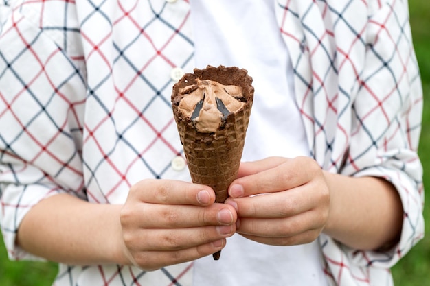 Le mani del bambino che tengono il gelato color cioccolato in un cono di waffle all'aperto in estate