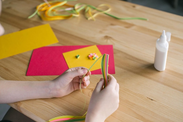 Le mani del bambino creano una carta con strisce colorate lunghe e strette di carta per quilling