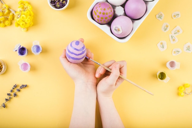 Le mani del bambino decorano le uova di pasqua sulla foto gialla di alta qualità del concetto di buona pasqua