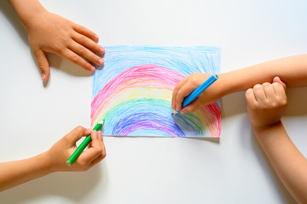 Le mani del bambino disegnano insieme le matite colorate arcobaleno su bianco