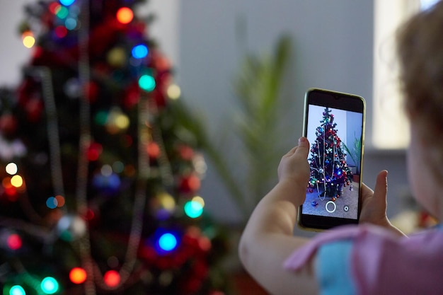 Le mani del bambino scattano foto o video utilizzando il telefono dell'albero di Natale alla vigilia di Natale.