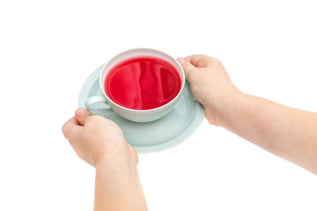 Le mani del bambino tengono la tazza di tè sul piattino isolato su bianco