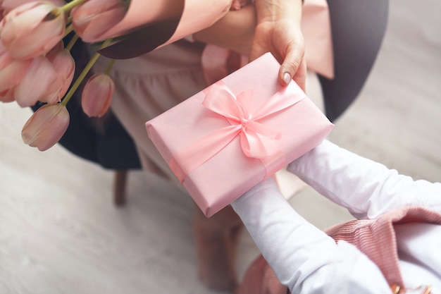 Le mani del bambino tengono una bella confezione regalo rosa con nastro e fiore di tulipano rosa. Vista dall'alto, primo piano. Preparazione per le vacanze.