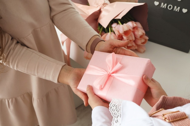 Le mani del bambino tengono una bella confezione regalo rosa con nastro. Fiore di tulipano rosa e segno ti amo mamma sullo sfondo. Vista dall'alto, primo piano. Preparazione per le vacanze.