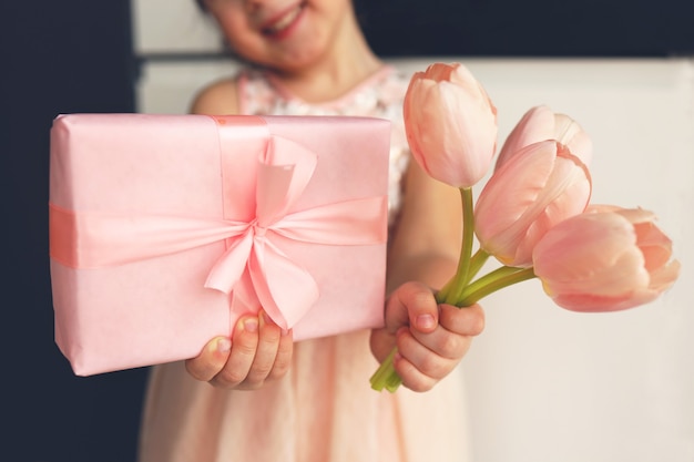 Le mani del bambino tengono una bella confezione regalo rosa con nastro. Fiore di tulipano rosa. Vista ravvicinata. Preparazione per le vacanze.