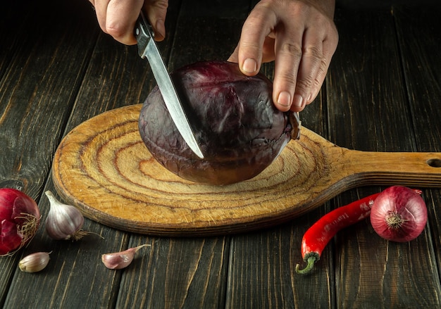 Le mani del cuoco stanno tagliando il cavolo rosso su un tagliere con un coltello