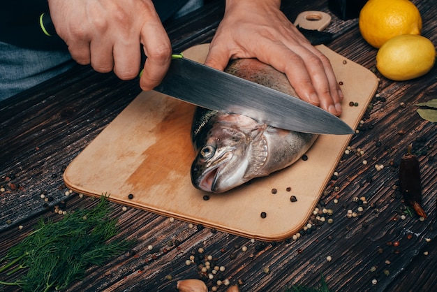 Le mani del cuoco unico con un taglio del coltello pescano su una tavola di legno nella cucina