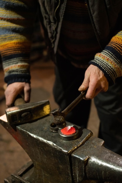 Le mani del fabbro lavorano con martelli su un'incudine con il primo piano in metallo caldo verticale