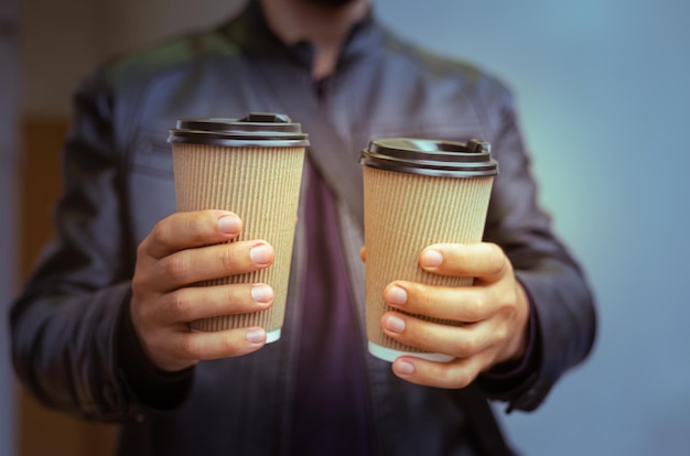 Le mani del giovane che tengono due tazze da caffè di carta usa e getta si chiudono per il freddo clima autunnale