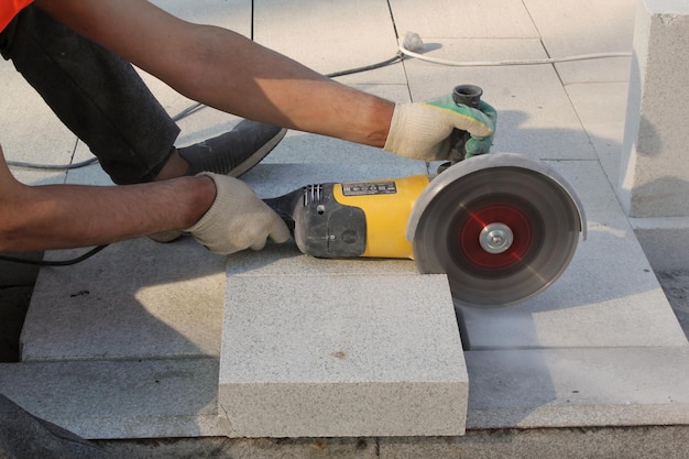 Le mani del lavoratore con la smerigliatrice elettrica rifiniscono le lastre di pavimentazione sul cantiere. Concetto di posa