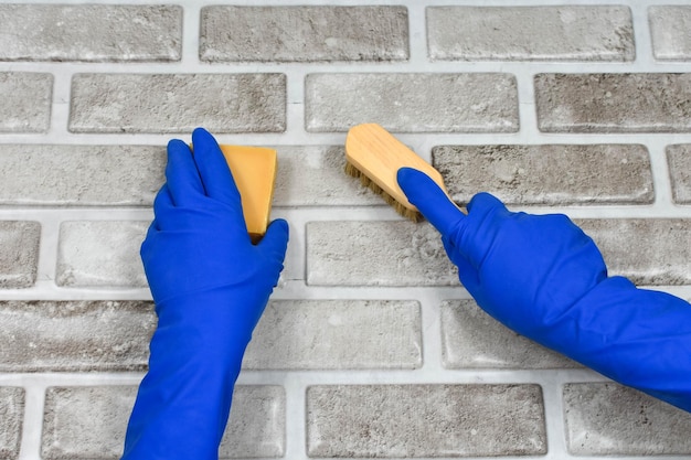 Le mani del lavoratore in guanti protettivi di gomma con uno straccio che puliscono la superficie di un tavolo o di una parete in una cucina del bagno della stanza Il concetto di pulizia