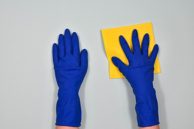 Le mani del lavoratore in guanti protettivi di gomma con uno straccio che puliscono la superficie di un tavolo o di una parete in una stanza bagno cucina Inizio primavera o pulizia regolare Il concetto di pulizia