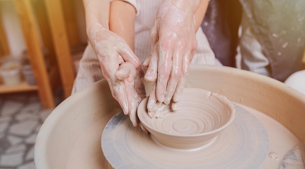 Le mani del maestro guidano le mani dell'apprendista che modellano un vaso di argilla su un tornio