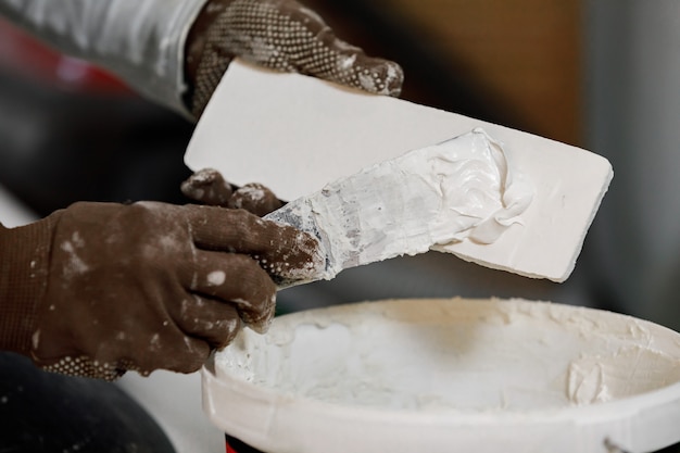 Le mani del maestro in guanti mettono la colla su un mattone decorativo prima dell'installazione su un muro